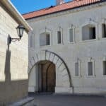 Ancient stone castle wall with archway and modern windows, featuring a classic streetlamp and red tiled roof.